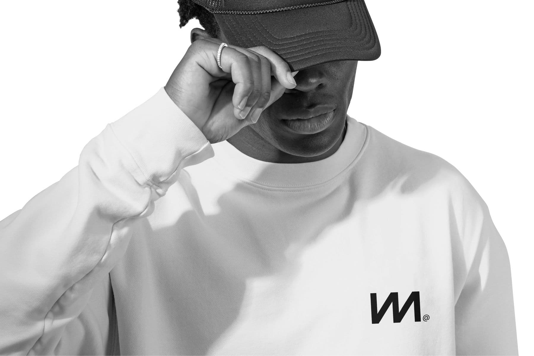 A man in the chalk Crew Sweatshirt and a cap, the M printed small on the chest
