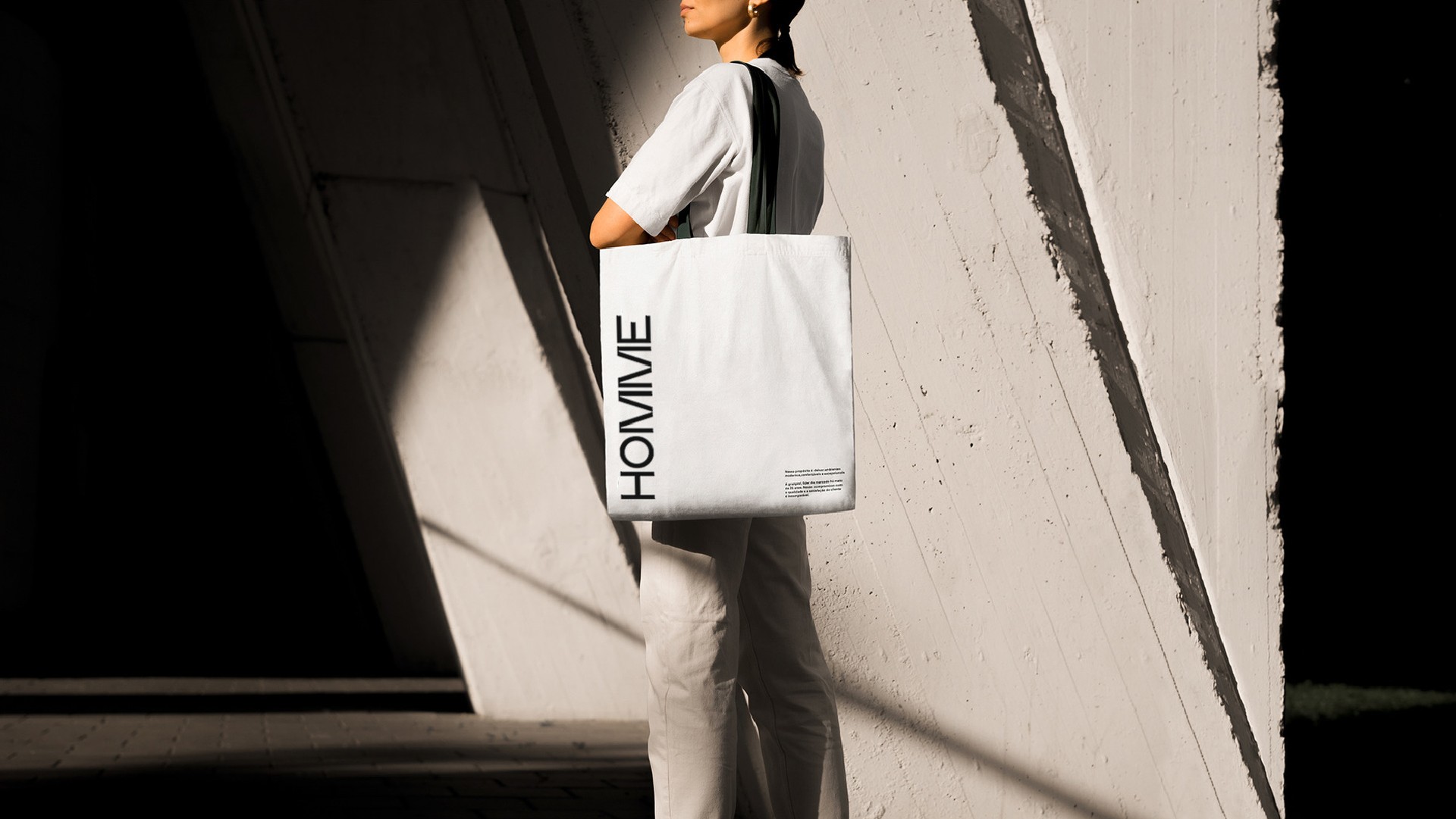 A person carrying a white Homme tote bag past a concrete wall