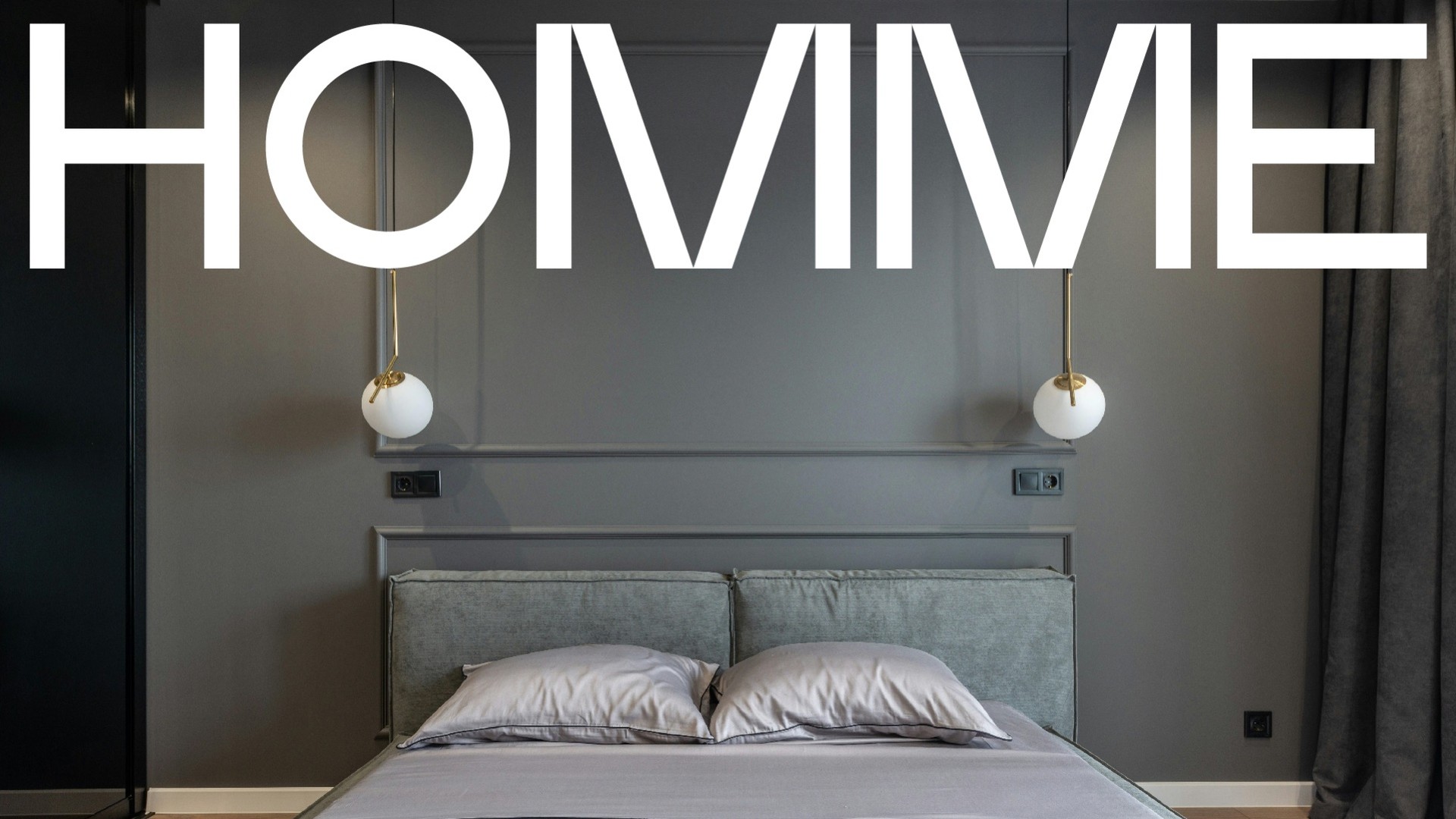 The Homme wordmark in white across a grey bedroom wall with two globe lamps