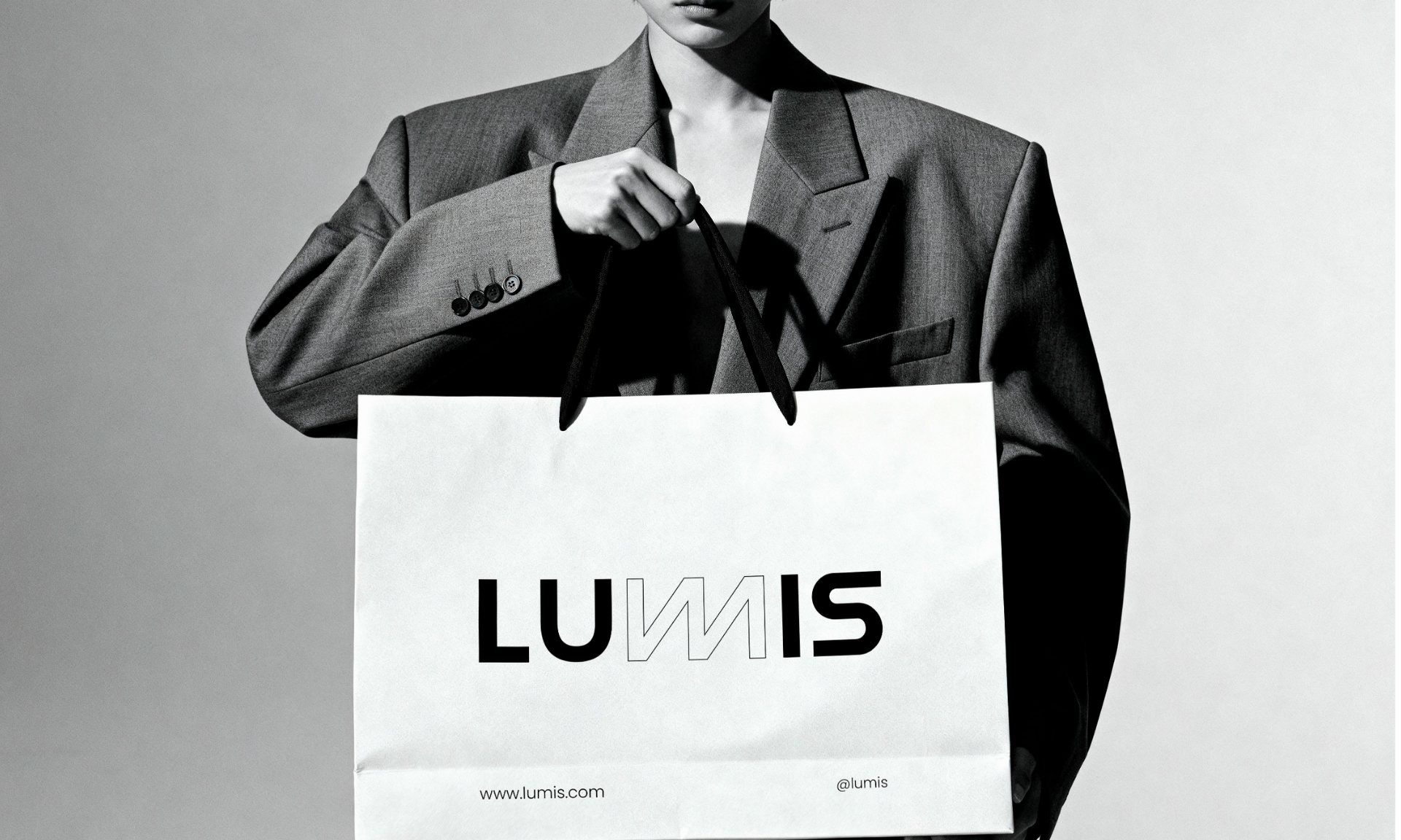 A person in a grey suit holding a white Lumis shopping bag