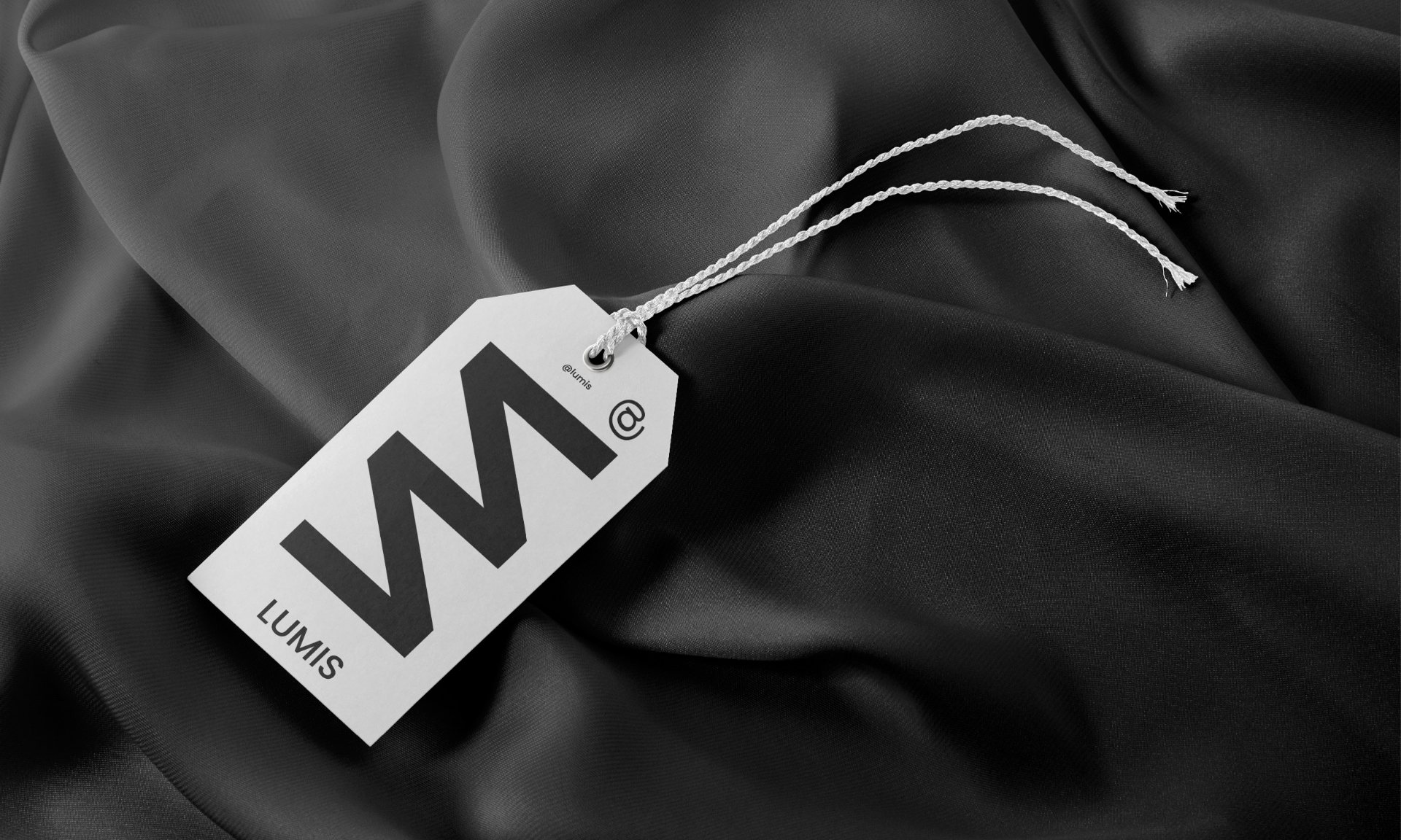 A grey Lumis swing tag with a large M on dark fabric