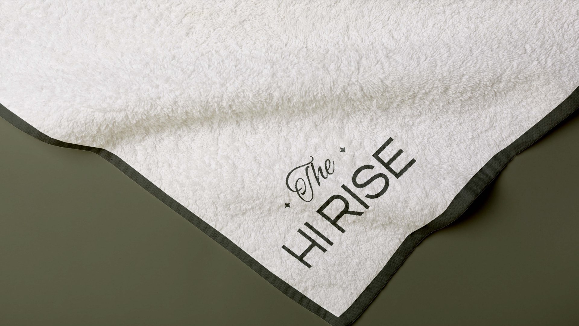 A white towel embroidered with the wordmark on olive