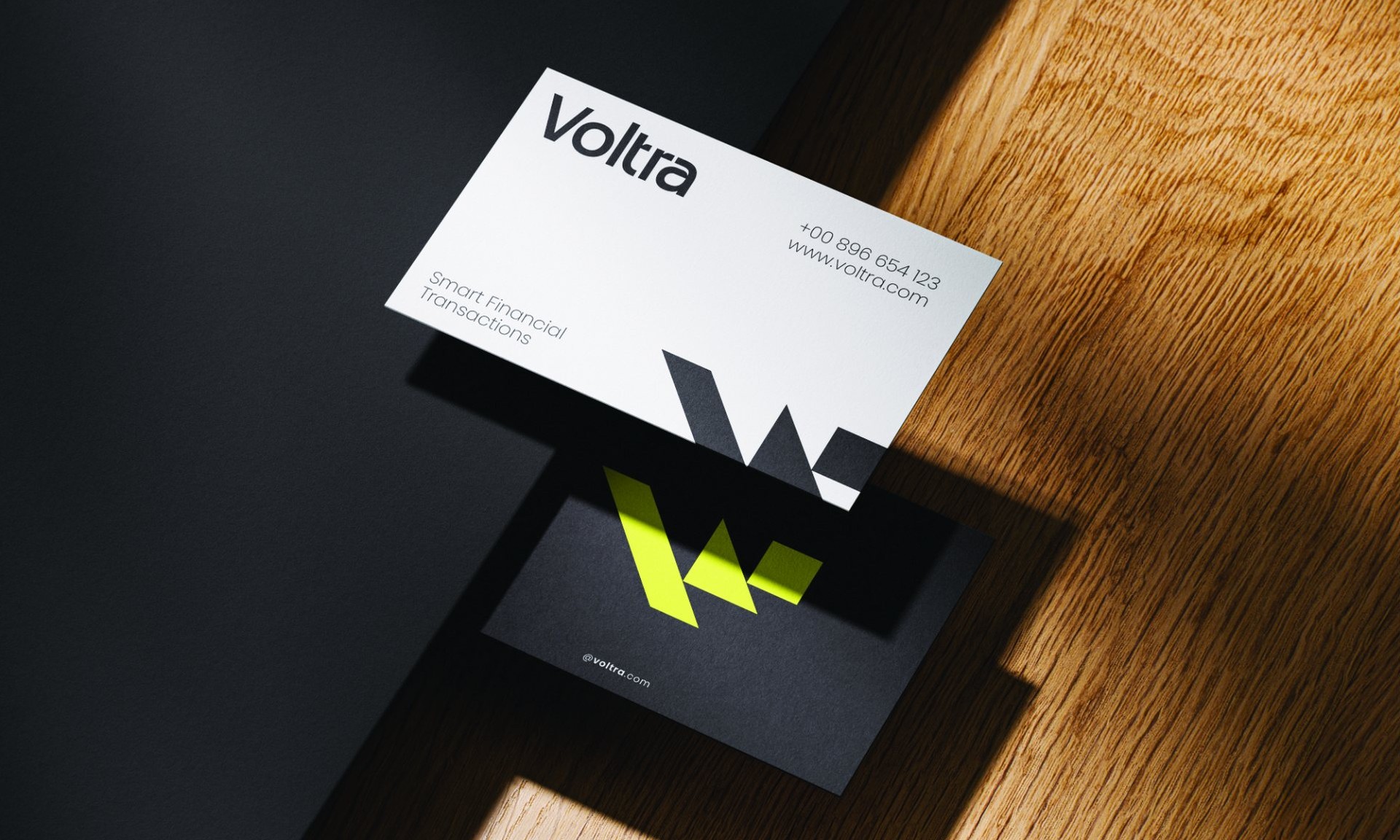 White and black Voltra business cards on a wooden desk in sunlight