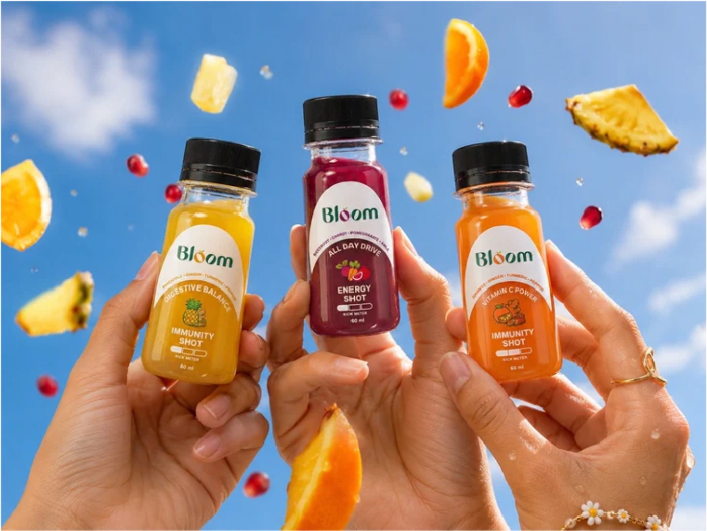 Three hands raising Bloom shots against a blue sky with flying fruit