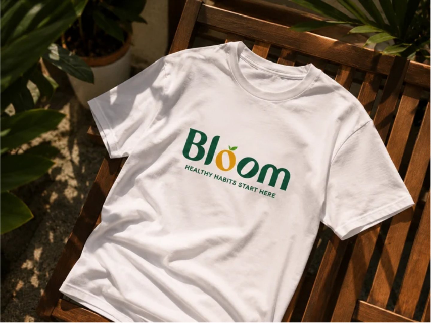 A white T-shirt with the Bloom wordmark on a wooden bench