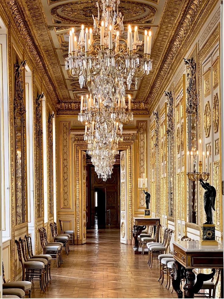 A tall gold room lined with mirrors, statues and chandeliers