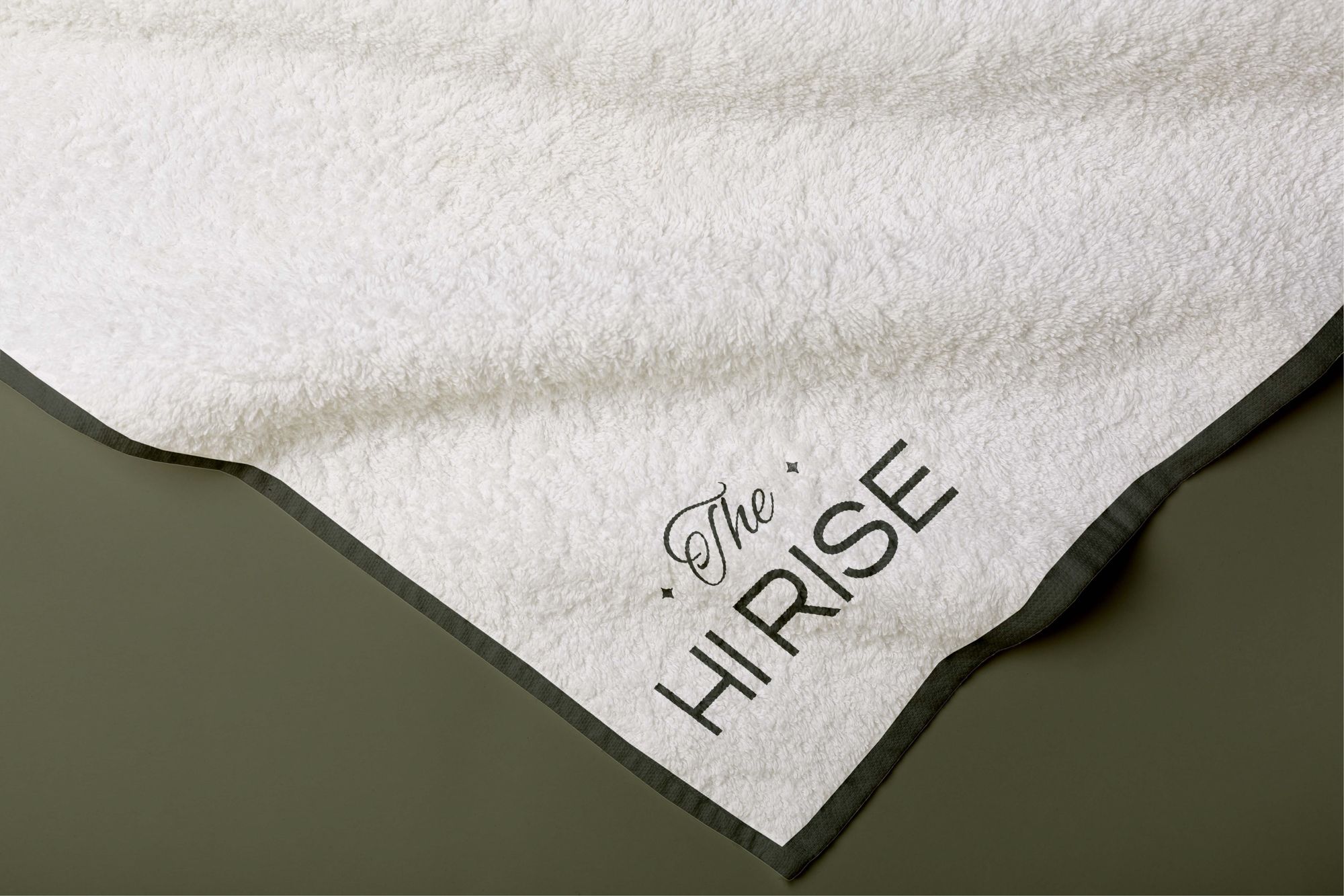 A white towel corner with The Hi Rise stitched in olive